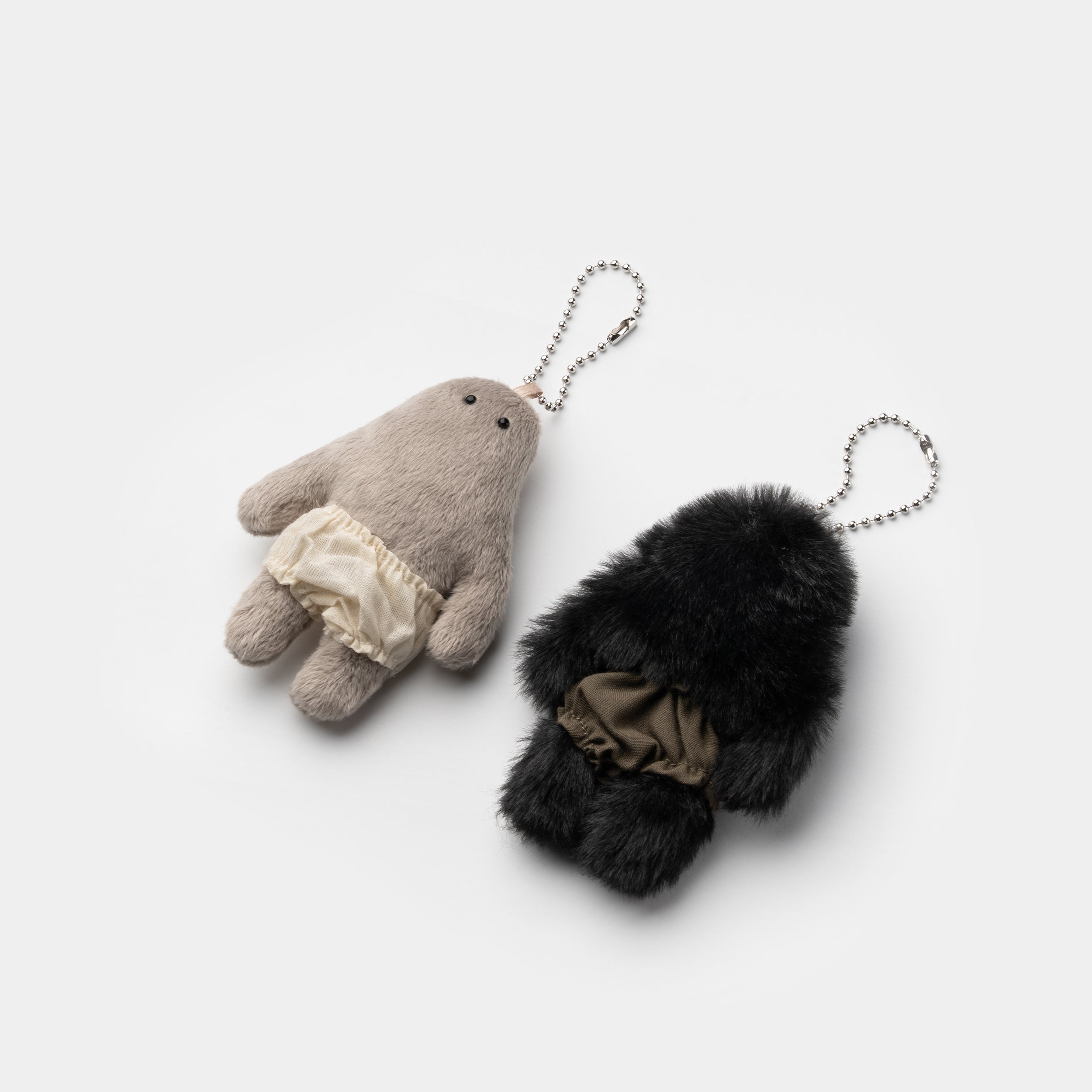 Opantsu-kun and MOU keychains displayed on a white surface, laying on their backs.